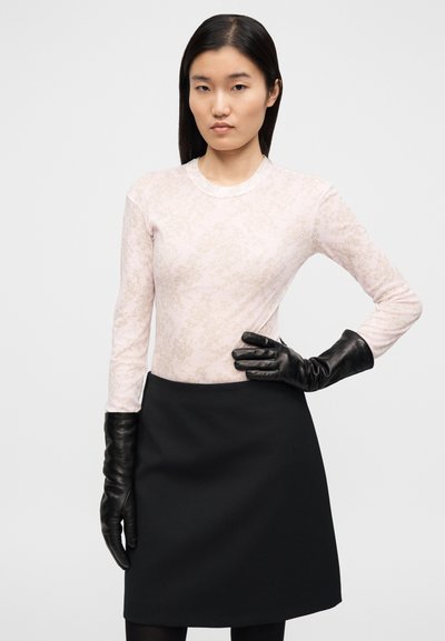 Μακρυμάνικο ανοιχτό ροζ τοπ με λουλουδάτο σχέδιο, συνδυασμένο με μαύρη φούστα και μακριά μαύρα δερμάτινα γάντια. Απλός, εφαρμοστός σχεδιασμός.