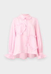 Ροζ ανοιχτόχρωμο μακρυμάνικο πουκάμισο με κουμπιά, με βολάν στο γιακά, στις μανσέτες και δύο μεγάλα βολανωτά μπαλώματα σε σχήμα καρδιάς στο μπροστινό μέρος.