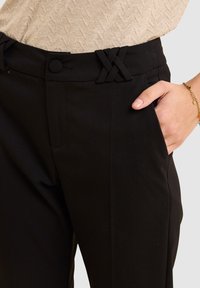 Pantalons noirs sur mesure avec un accent tissé à la taille, des poches latérales et une texture de tissu lisse et élégante.