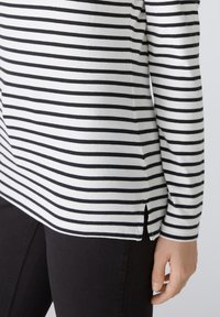 Gestreepte lange mouw top in wit en zwart katoen, met zijsplitten aan de zoom, gecombineerd met zwarte broek. Gladde textuur.