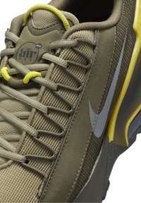 Olivgrön sneaker med en texturerad meshovandel, grå swoosh och gula snören. Har en vadderad krage och en slitstark gummisula.