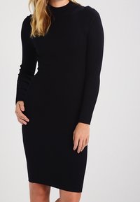 Zwarte geribbelde jurk met lange mouwen, een aansluitend silhouet, een ronde halslijn en een midilengte zoom. Gladde textuur, zonder zichtbare patronen of accenten.