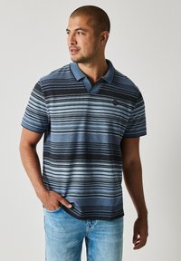Pruhovaná polo tričko v odstínech modré a černé, vyrobené z texturovaného materiálu, s kontrastním modrým límečkem a kulatou nášivkou s logem.
