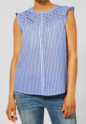 Mouwloze blouse met verticale blauwe en witte strepen, knoopsluiting en kanten ooglet inzetstuk, gedragen met een blauwe spijkerbroek.