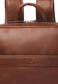 Bruine leren rugzak met een gladde textuur, dubbele bandjes, bovenhandvat en een ritssluiting met subtiele merkdetails en stikaccenten.