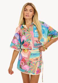 Ensemble de chemise à manches courtes colorées et de jupe portefeuille présentant des motifs tropicaux, des bords festonnés et diverses couleurs pastel. Tissu léger.