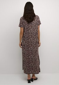 Kevyt maxi-mekko, jossa on leopardi-kuosi ruskean ja mustan sävyissä, lyhyet hihat ja sivuhalkiot liikkumisen helpottamiseksi.