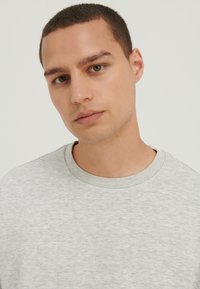 Lys grå crewneck genser i myk stoff. Har et enkelt design med ribbet krage og ingen synlige mønstre eller detaljer.