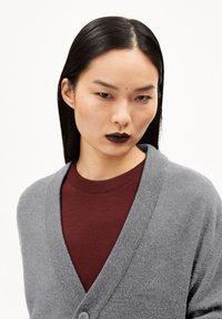 Gray knitted cardigan with a V-neck and button closure, worn over a maroon crew-neck shirt. Features an embroidered detail on the chest.