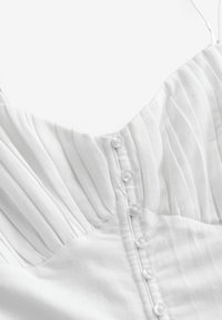 Hvid kjole med plisseret bodice, justerbare stropper og knaplukning bagpå. Glat stof med en blød tekstur.
