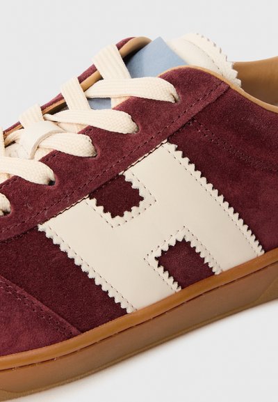 Sneaker in suede bordeaux con dettagli in pelle crema, caratterizzato da design testurizzati e lacci beige, e una suola in gomma naturale.