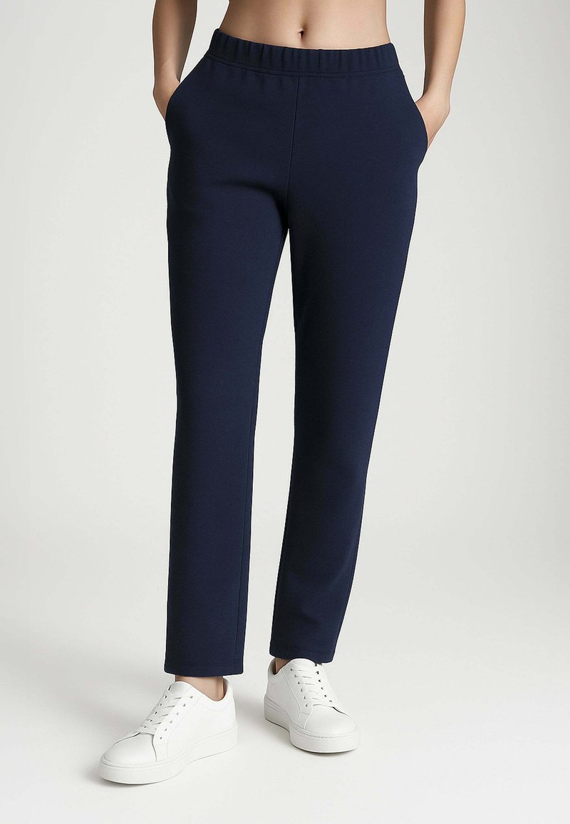 Pantaloni jogger blu navy con elastico in vita, tasche laterali e design a gamba dritta, abbinati a sneaker bianche. Materiale morbido e elasticizzato.