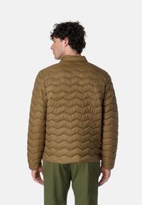 Giacca a cosciali marrone con colletto alto, caratterizzata da un motivo a zigzag texturizzato, abbinata a pantaloni verdi, vista da dietro.