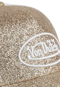 Gold glitter baseball cap with a white embroidered "Von Dutch" logo. The surface has a textured, sparkling finish.