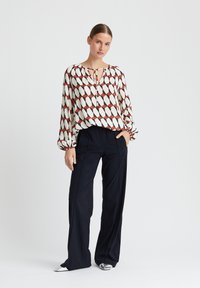 Langarm blouse met een crème basis, een rood en zwart ruitpatroon en een keyhole halslijn. Gecombineerd met hoge zwarte broek en zilveren schoenen.