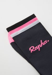 Calcetín de ciclismo negro con rayas rosas, grises y blancas en el puño. Presenta un tejido texturizado y el logo bordado "Rapha" en rosa.