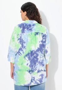 Camisa ligera en un patrón de teñido anudado en azul, verde y blanco. Presenta un cuello, mangas de tres cuartos y un detalle de pliegues en la parte posterior.