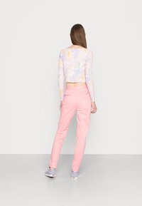 Long-sleeved, cropped top in pastel tie-dye pattern, paired with light pink trousers. The outfit has a casual cut, emphasizing comfortable wear.