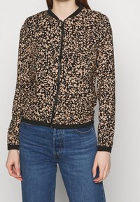 Veste bomber à motif abstrait beige et noir, dotée d'une fermeture éclair frontale, de poignets et d'un ourlet côtelés, confectionnée en tissu léger pour le confort.