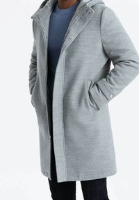 Abrigo gris claro con capucha, hecho de tela texturizada, con cremallera frontal, bolsillos laterales y diseño de ajuste relajado.