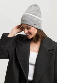 Hallide hallgatav beige, valge triibuga, valmistatud pehmest kangast. Omab soonikkoes tekstuuri ja väikest pruuni logo aksenti.