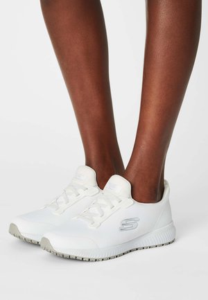 Scarpe da ginnastica bianche con tomaia in tessuto testurizzato, punta rotonda e suola in gomma spessa. Le caratteristiche includono lacci e un logo sul lato.