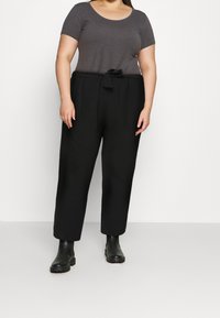 Pantalons noirs avec une taille nouée, associés à un haut gris ajusté à manches courtes. Le modèle porte des bottes noires à la cheville. Texture de tissu lisse.