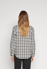 Sort-hvid ternet bluse med lange ærmer, afslappet pasform og rund kant, fremstillet af tekstureret stof.