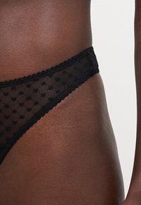 Svart blondertring med prikkete mønster, med bølgede kanter og en glatt midjebånd. Designet for komfort og en slank passform.