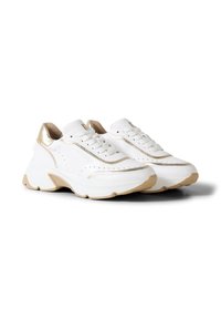 Bílé masivní tenisky s béžovými podrážkami a zlatými detaily kolem paty, tkaniček a špičky, zobrazené jako pár na bílém pozadí.