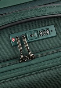 Groene reis-suitcase met een textuurstofoppervlak, dubbele beveiligingsritsen en een ingebouwd combinatie-slot. Merk duidelijk zichtbaar.