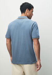 Blå pikétröja med en subtil textur, utrustad med en klassisk krage och kontrasterande randiga detaljer på kragen och ärmarna.