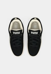 Black sneakers made of fabric with a textured surface, featuring dark laces, a beige sole, and "PUMA" branding on the tongue and side.
