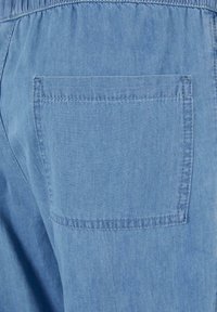 Světle modrá riflovina s obdélníkovým zadním kapsou s viditelnými švy na volných kalhotách.