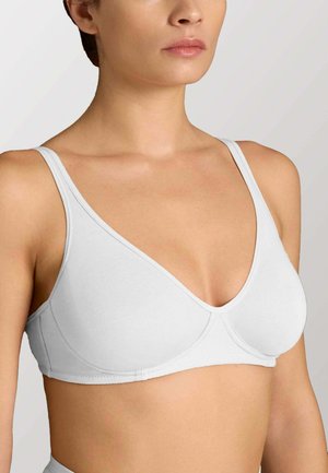 Donna che indossa un reggiseno bianco semplice, leggermente imbottito, con spalline sottili e scollo a V profondo, mostrata dalle spalle alla vita.