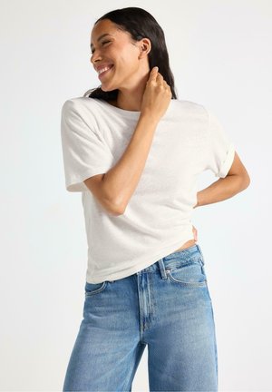 T-shirt bianco in cotone con maniche arrotolate abbinato a jeans in denim azzurro chiaro. La maglietta ha una vestibilità comoda e una texture morbida.