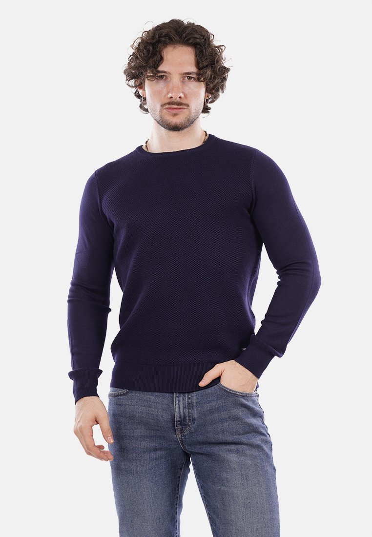 Maglione lavorato a maglia blu navy con maniche lunghe, scollatura a girocollo e polsini e orlo a coste. Indossato con jeans azzurri.