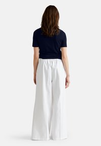 Námořnický modrý top s krátkým rukávem v kombinaci s bílými širokými kalhotami. Kalhoty mají elastický pas a hladký, lehký materiál.