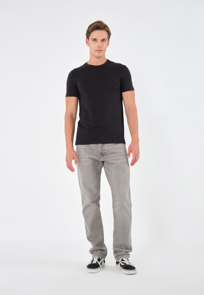 T-shirt nera a maniche corte abbinata a jeans grigio chiaro, con una vestibilità classica e design minimalista, con sneakers bianche e nere.