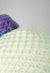 Knit beanie in light yellow, featuring a textured pattern. Accented with a colorful pom-pom in teal and pink at the top.