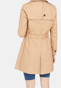 Beżowy trencz z paskiem w talii, podwójnym zapięciem z przodu i naramiennikami. Posiada plisowany tył i akcenty w postaci guzików.