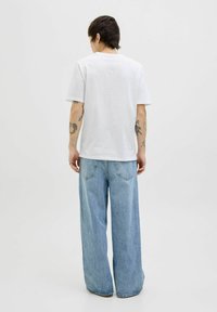 Tricou alb din bumbac, cu mâneci scurte și guler rotund, asortat cu blugi din denim cu picioare largi, de culoare bleu deschis, cu buzunare la spate.