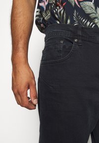 Mörka denimjeans med en slät textur; funktioner inkluderar knappknäppning, fem fickor och en åtsittande design med minimal söm-detall.