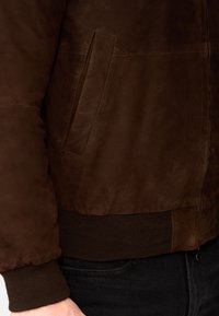 Brown suede bomber jacket featuring a ribbed knit hem and cuffs, with a zip closure and side pocket detail.