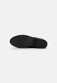 Botine negre până la gleznă, cu un brâu neted, vârf rotund și talpă din cauciuc texturat și plat. Prezintă detalii subtile cu logo pe talpa exterioară.