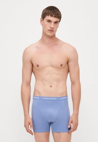 Blaue Baumwoll-Boxershorts mit weicher Textur, die einen weißen "BJÖRN BORG"-Logo-Bund und eine enge Passform aufweisen. Keine Muster oder zusätzlichen Details.