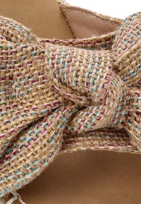 Sandalias de color marrón tejido con un detalle de lazo, que cuentan con hilos multicolores entrelazados en la tela similar a yute. Plantilla suave en tono marrón.