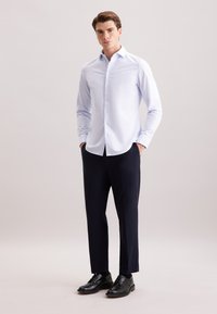 Camicia azzurro chiaro a maniche lunghe con colletto button-down, abbinata a pantaloni blu scuro e scarpe in pelle nera. Tessuto morbido, vestibilità su misura.