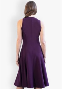 Une robe sans manches de couleur violette avec un corsage ajusté et une jupe évasée, fabriquée dans un tissu lisse de couleur unie et avec des coutures minimales.