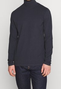 Mörk marinblå långärmad polotröja i mjukt material, med en åtsittande passform, slät textur och minimala sömdetaljer. Avslappnad design.